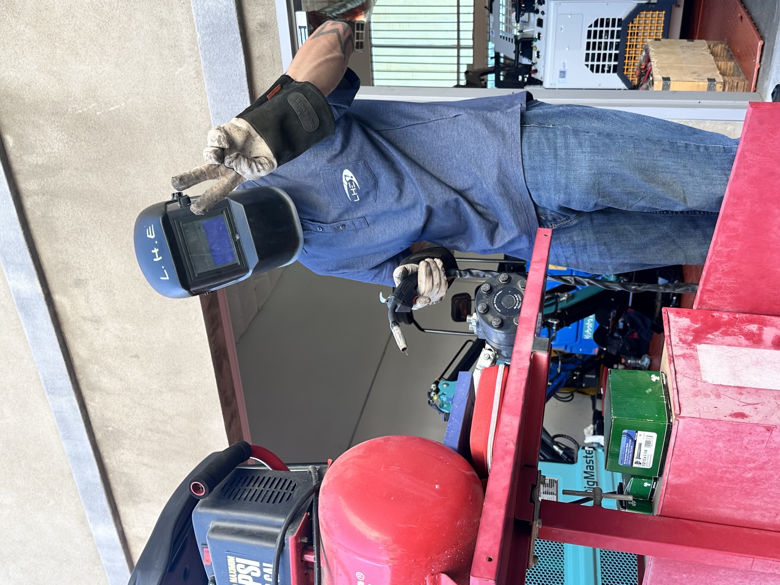 A Leon's Heavy Equipment technician wearing a welding helmet beside shop equipment.