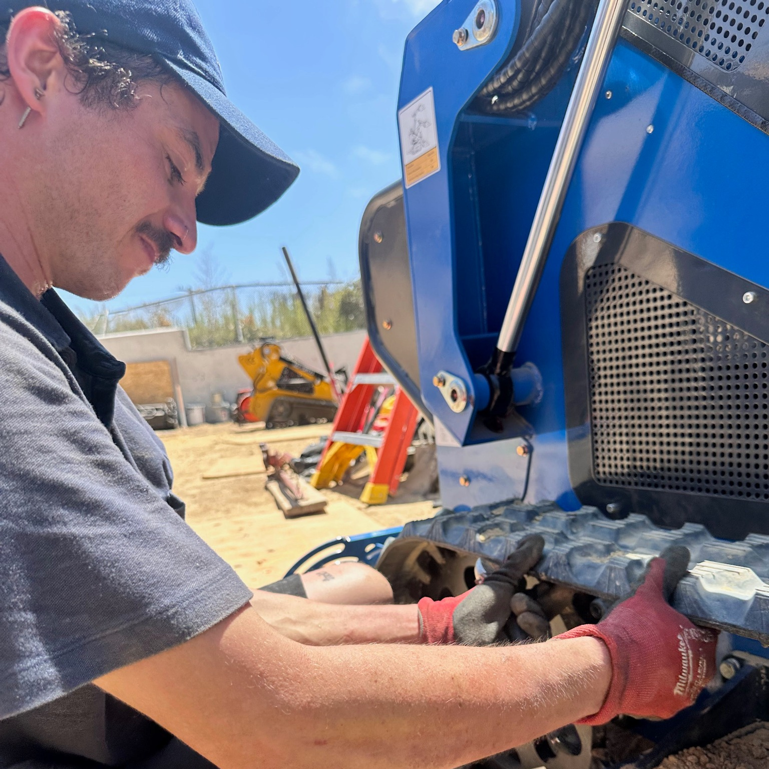 A Leon's Heavy Equipment technician servicing a compact blue machine outdoors.
